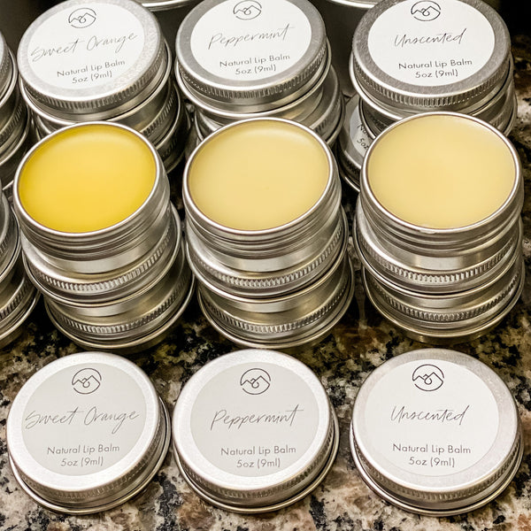 Stacks of closed and open lip balm tins in three scents: Sweet Orange, Peppermint, and Unscented