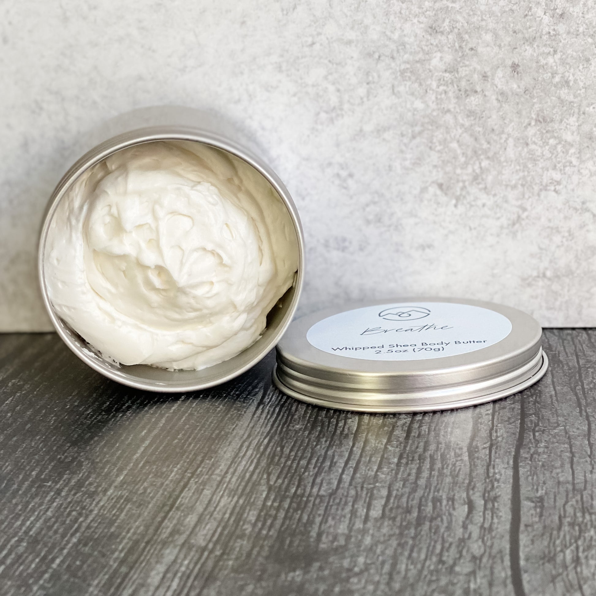 Breathe Whipped Body Butter in open tin turned on its side with lid next to it. Displays how thick and rich this body butter is.