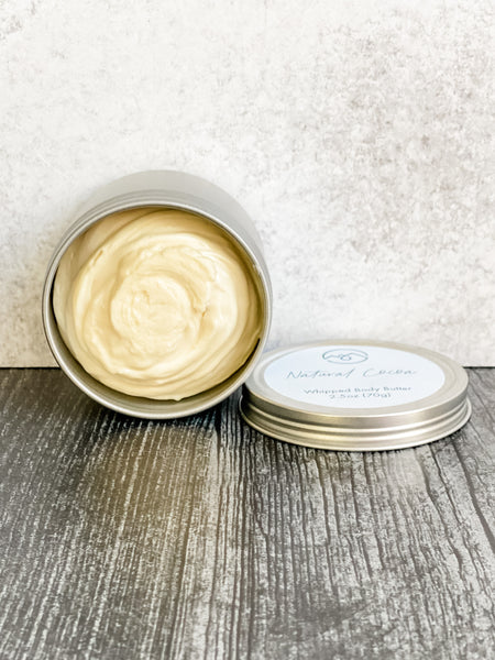 Natural Cocoa Whipped Body Butter in open tin turned on its side with lid next to it. Displays how thick and rich this body butter is.